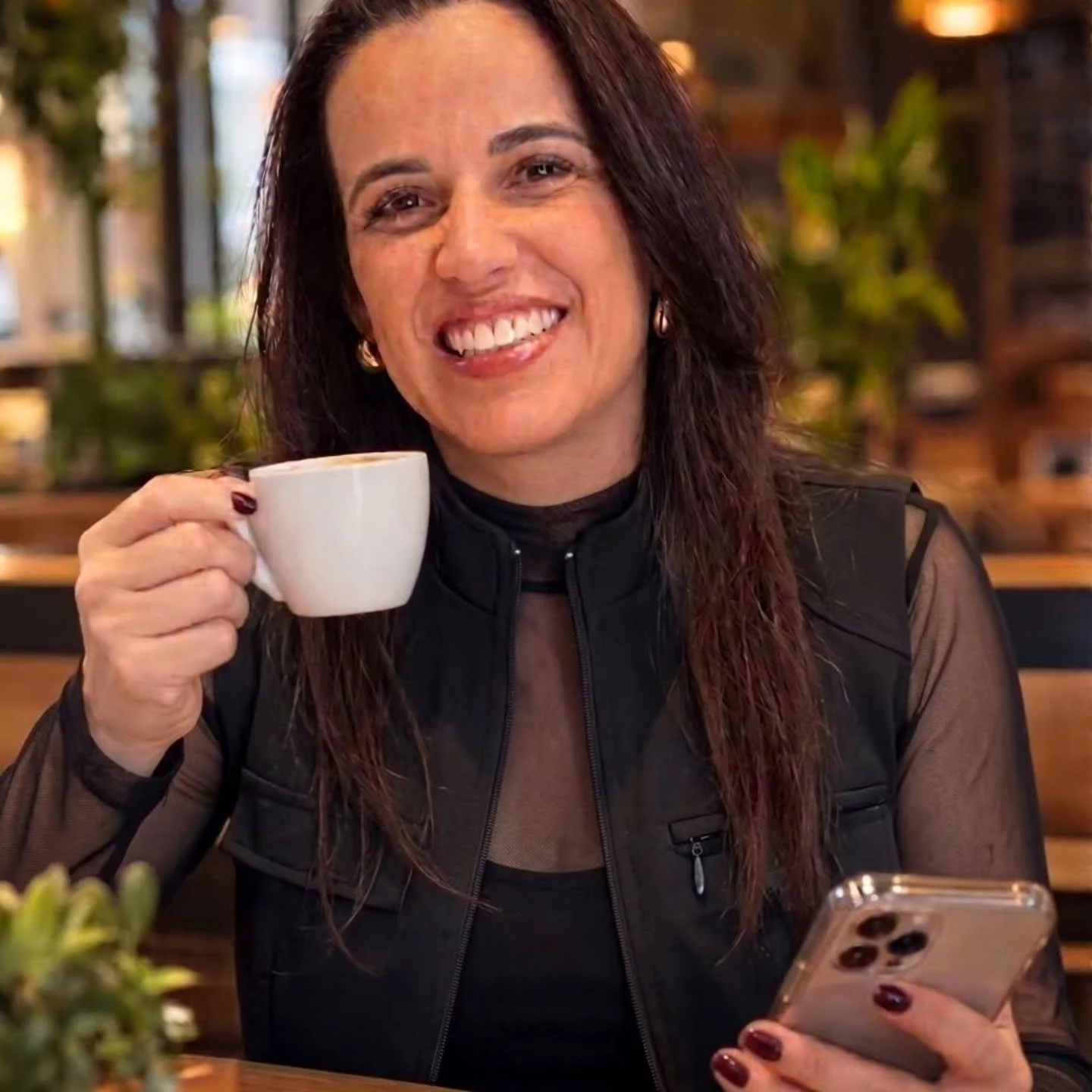 Dra. Kelli Marques rindo, com uma xícara de café na mão, numa cafeteria